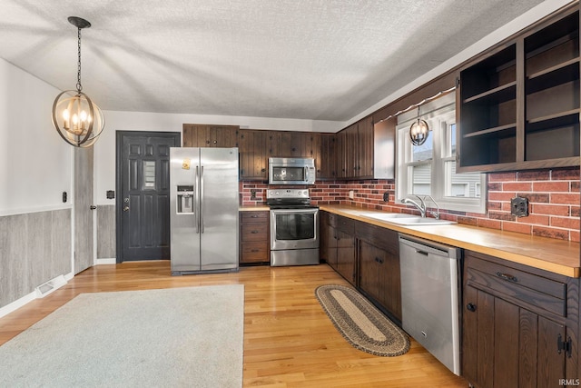 kitchen with sink, hanging light fixtures, stainless steel appliances, a textured ceiling, and light wood-type flooring