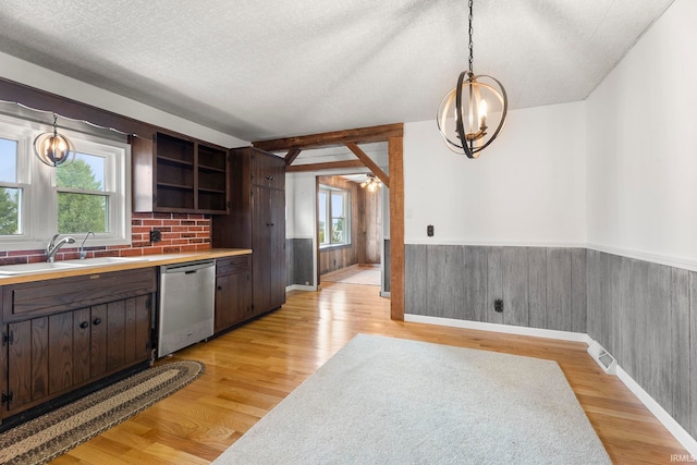 kitchen featuring a textured ceiling, dishwasher, light hardwood / wood-style floors, hanging light fixtures, and wood walls