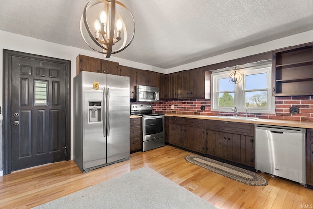 kitchen featuring stainless steel appliances, sink, decorative light fixtures, an inviting chandelier, and light hardwood / wood-style floors