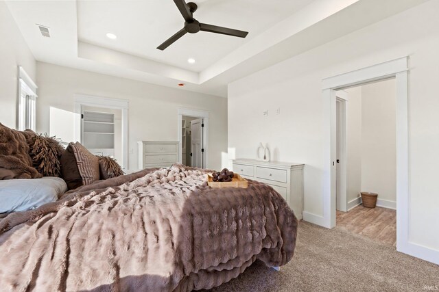 bedroom featuring ceiling fan, a raised ceiling, a spacious closet, and light carpet