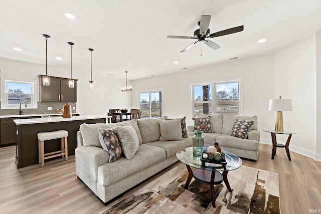 living room featuring ceiling fan with notable chandelier, light hardwood / wood-style floors, and sink