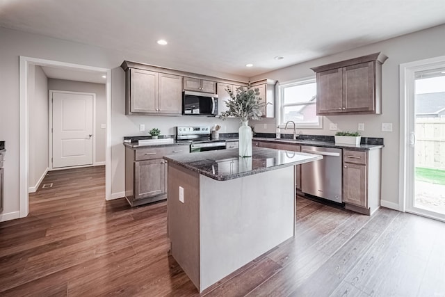 kitchen featuring appliances with stainless steel finishes, dark hardwood / wood-style flooring, dark stone counters, sink, and a kitchen island