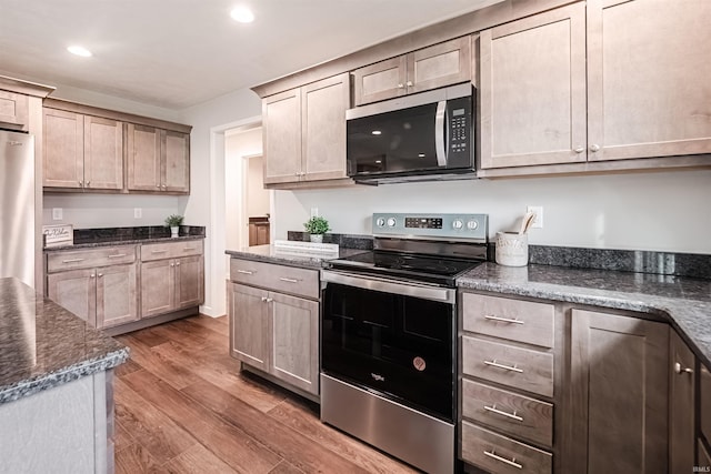 kitchen featuring hardwood / wood-style floors, stainless steel appliances, and dark stone counters