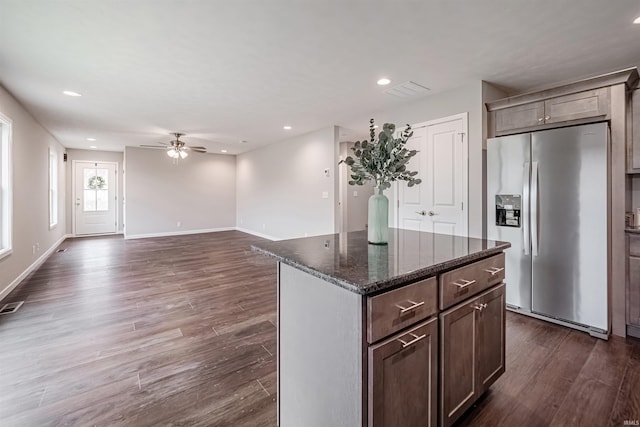 kitchen with a center island, dark wood-type flooring, dark stone counters, ceiling fan, and stainless steel fridge with ice dispenser