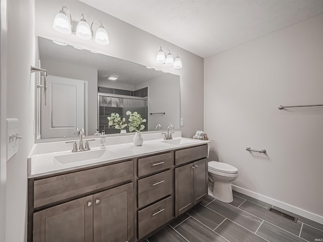 bathroom with a textured ceiling, vanity, toilet, and a shower with shower door