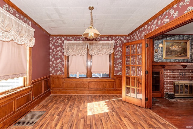 unfurnished dining area featuring hardwood / wood-style floors, crown molding, and a fireplace