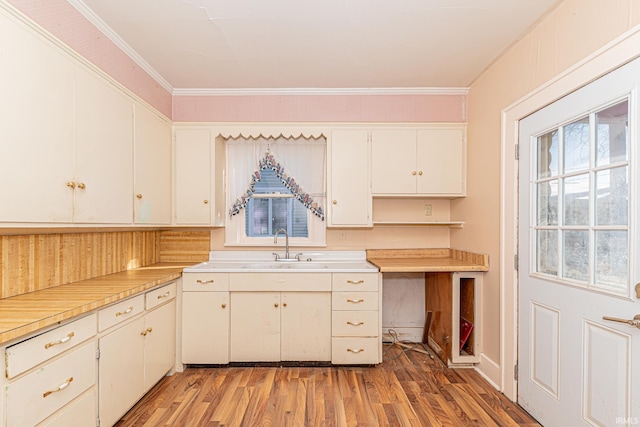 kitchen with white cabinets, wood-type flooring, crown molding, and sink