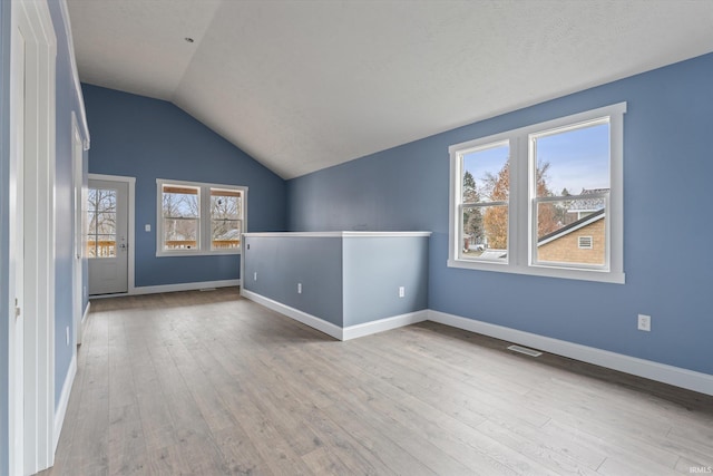 spare room featuring a textured ceiling, light hardwood / wood-style flooring, and lofted ceiling