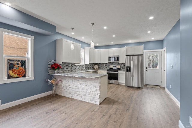 kitchen with light hardwood / wood-style flooring, kitchen peninsula, decorative light fixtures, white cabinets, and appliances with stainless steel finishes