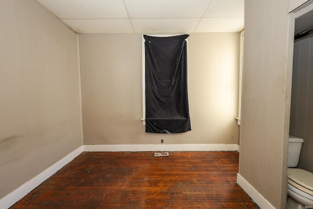 empty room with a paneled ceiling, wooden walls, and dark hardwood / wood-style floors