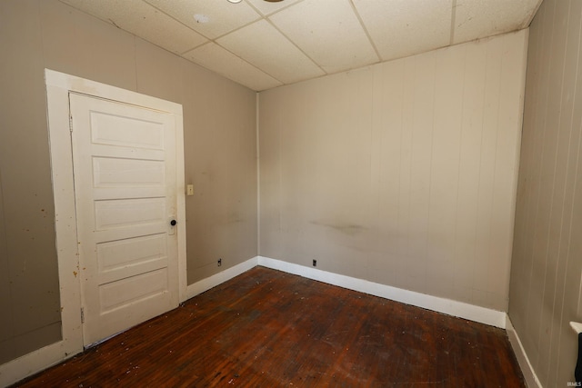 unfurnished room with a paneled ceiling, wood walls, and dark hardwood / wood-style flooring