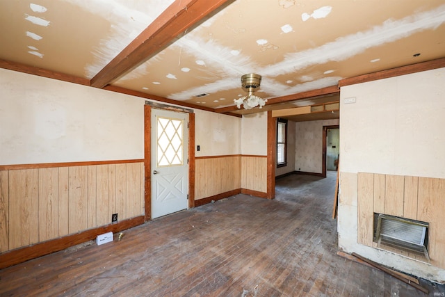 empty room featuring a fireplace, ceiling fan, wooden walls, dark wood-type flooring, and beamed ceiling