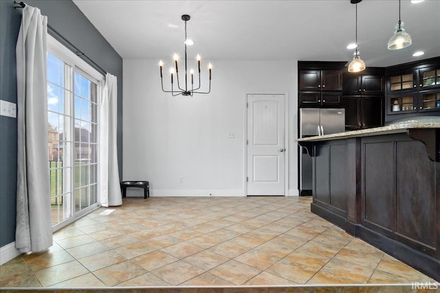 kitchen featuring stainless steel fridge, light stone counters, dark brown cabinets, decorative light fixtures, and an inviting chandelier