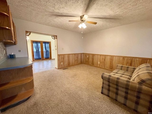 unfurnished room featuring ceiling fan, wooden walls, light colored carpet, and a textured ceiling