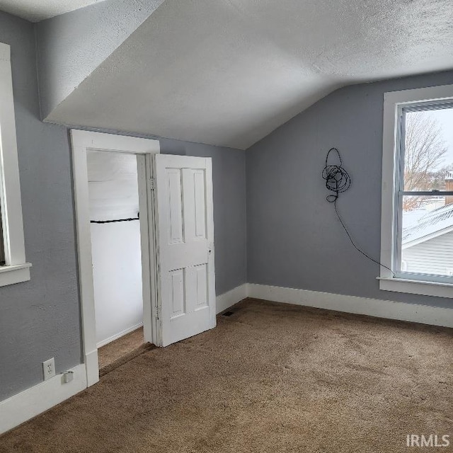 unfurnished bedroom with carpet flooring, a textured ceiling, and vaulted ceiling