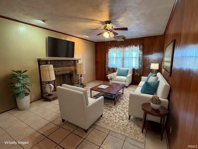 living room featuring ceiling fan, a stone fireplace, crown molding, wooden walls, and light tile patterned floors