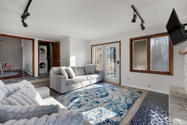 living room with stacked washer / dryer, a healthy amount of sunlight, track lighting, and wood-type flooring