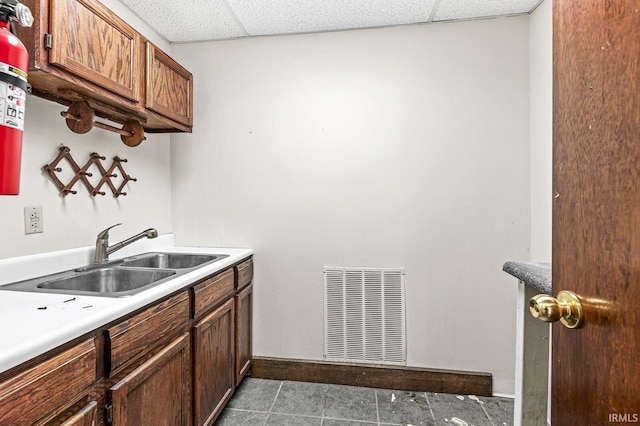 kitchen featuring dark tile patterned flooring, a drop ceiling, and sink