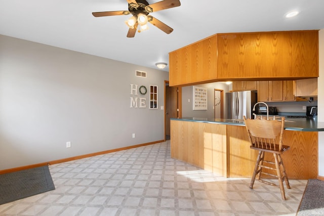 kitchen featuring ceiling fan, kitchen peninsula, a breakfast bar area, and stainless steel refrigerator