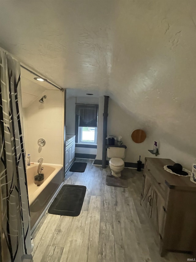 bathroom featuring toilet, hardwood / wood-style floors, lofted ceiling, and shower / tub combo with curtain