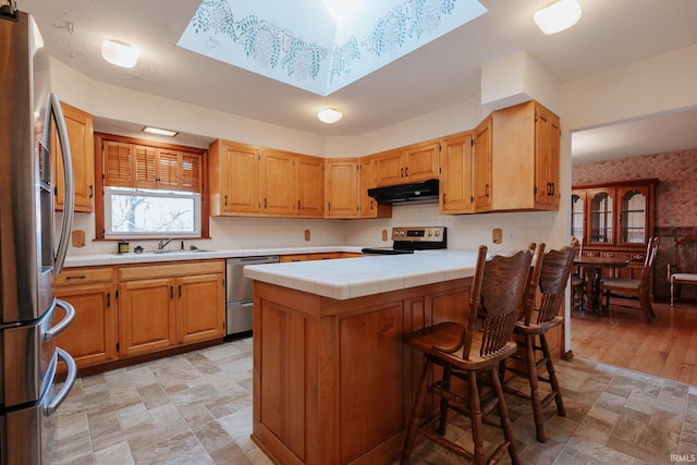 kitchen with decorative backsplash, appliances with stainless steel finishes, tile countertops, and a skylight