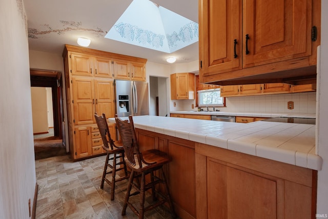 kitchen with decorative backsplash, a skylight, stainless steel appliances, sink, and tile counters