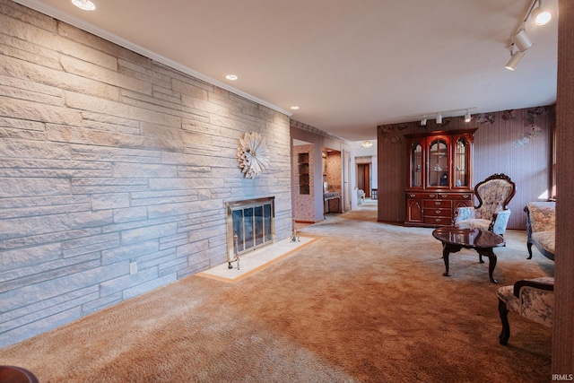 living room with carpet, rail lighting, a stone fireplace, and crown molding