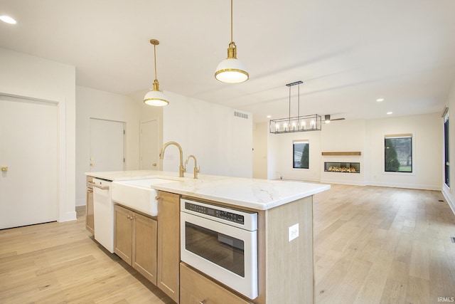 kitchen featuring pendant lighting, an island with sink, light hardwood / wood-style floors, and white appliances