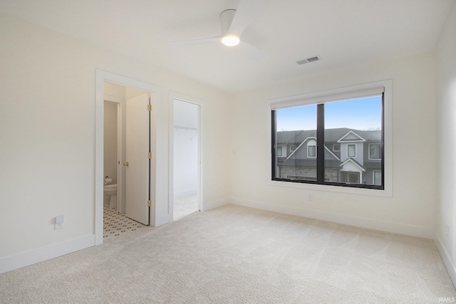 unfurnished bedroom featuring ensuite bath, a spacious closet, ceiling fan, light carpet, and a closet