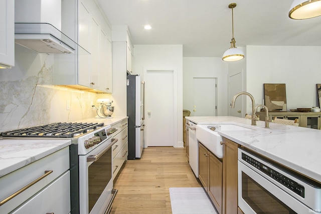 kitchen featuring light wood-type flooring, light stone counters, white appliances, wall chimney range hood, and white cabinetry