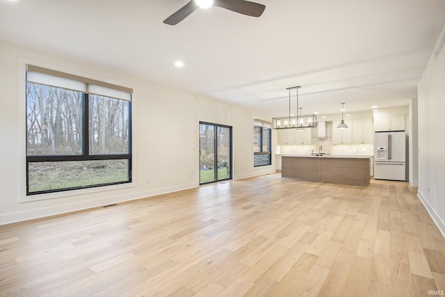 unfurnished living room with light wood-type flooring, sink, and a wealth of natural light