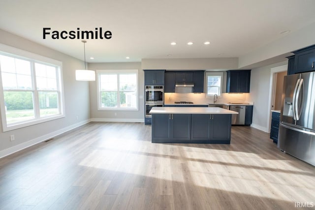 kitchen with appliances with stainless steel finishes, backsplash, pendant lighting, light hardwood / wood-style floors, and a kitchen island