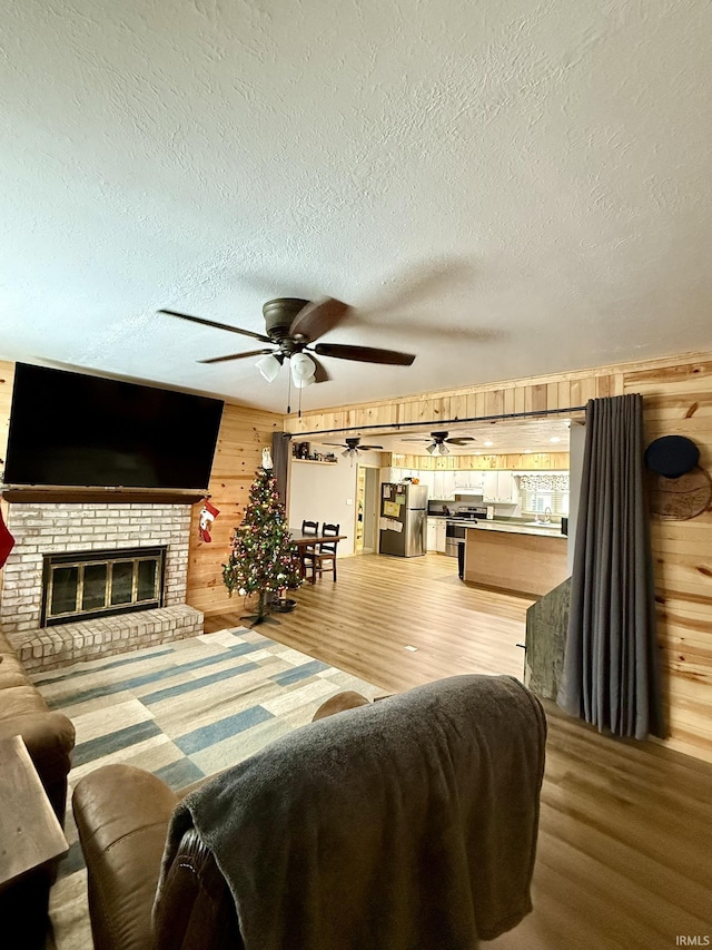 living room with a brick fireplace, wooden walls, a textured ceiling, and hardwood / wood-style flooring