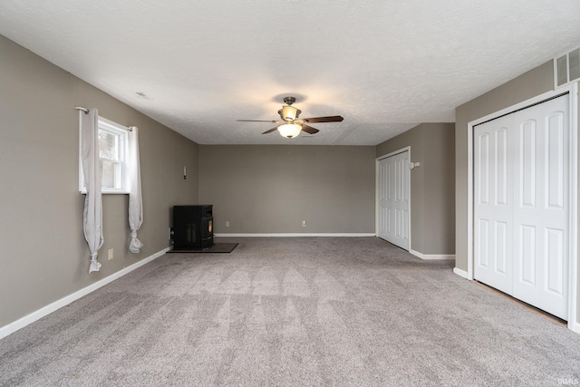 unfurnished living room with a wood stove, ceiling fan, light carpet, and a textured ceiling