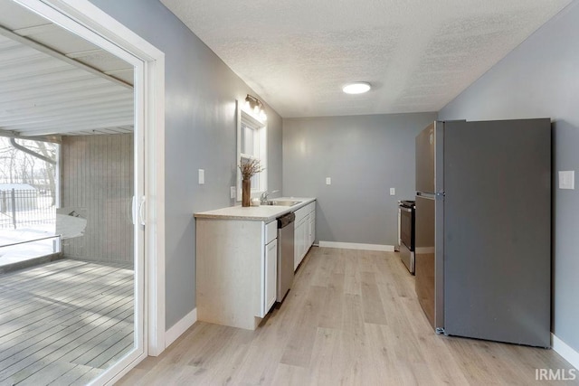 kitchen with a textured ceiling, stainless steel appliances, sink, light hardwood / wood-style flooring, and white cabinets