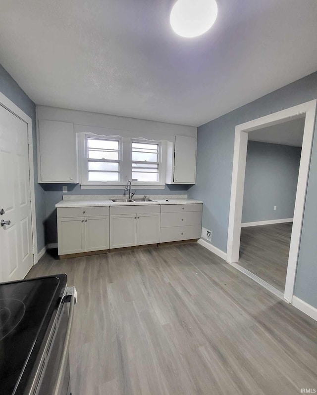 kitchen featuring stainless steel electric stove, white cabinetry, sink, and light hardwood / wood-style floors