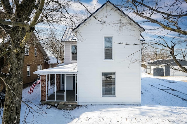 snow covered back of property featuring a sunroom