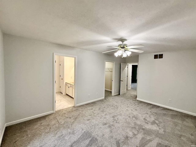 unfurnished bedroom with ceiling fan, ensuite bathroom, a textured ceiling, a walk in closet, and light colored carpet