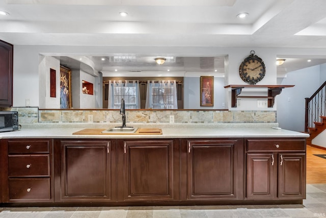 kitchen with dark brown cabinets, light wood-type flooring, a raised ceiling, and sink