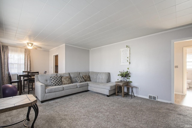 living room featuring carpet flooring, ceiling fan, ornamental molding, and a wealth of natural light