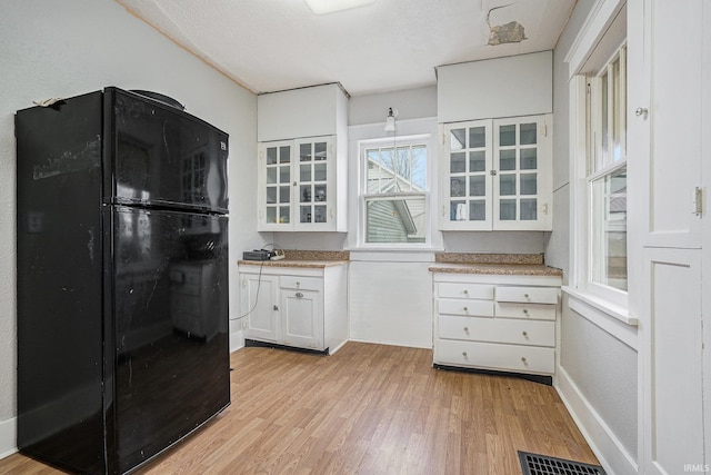 kitchen featuring white cabinets, black fridge, light wood-type flooring, and a textured ceiling