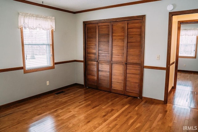 unfurnished bedroom with a closet, hardwood / wood-style floors, and ornamental molding