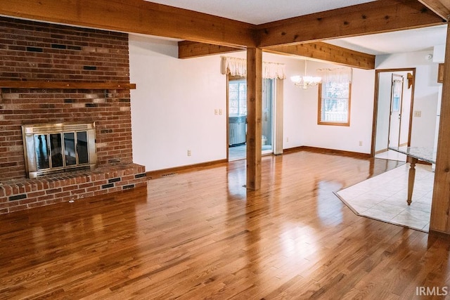 unfurnished living room with beamed ceiling, wood-type flooring, a fireplace, and a notable chandelier