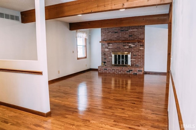 unfurnished living room with hardwood / wood-style flooring, beam ceiling, a textured ceiling, and a brick fireplace