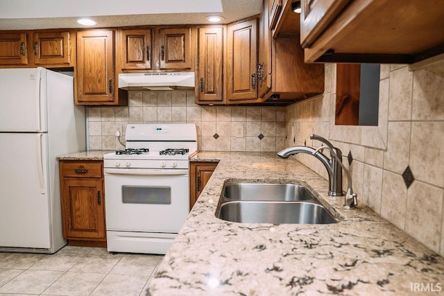 kitchen featuring sink, light stone counters, backsplash, white appliances, and light tile patterned floors