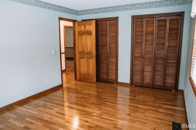 unfurnished bedroom with hardwood / wood-style floors, a textured ceiling, and two closets