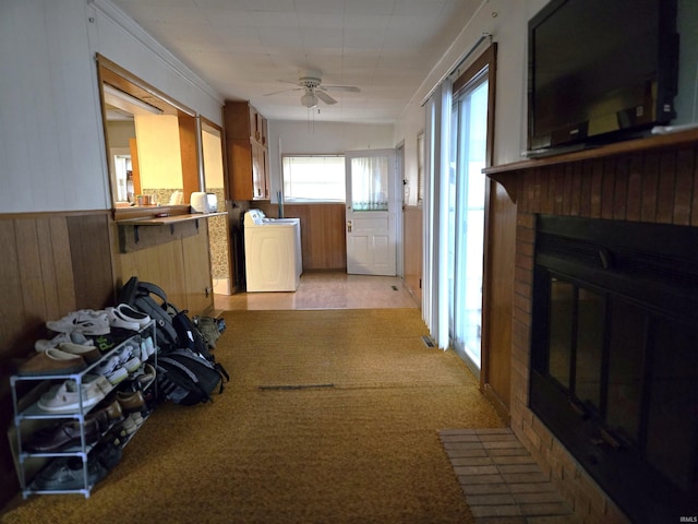 interior space featuring ceiling fan, a brick fireplace, washer / clothes dryer, wood walls, and light carpet