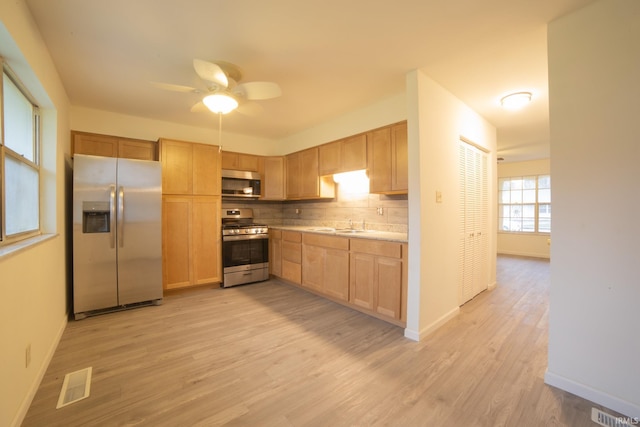 kitchen featuring ceiling fan, sink, stainless steel appliances, backsplash, and light wood-type flooring