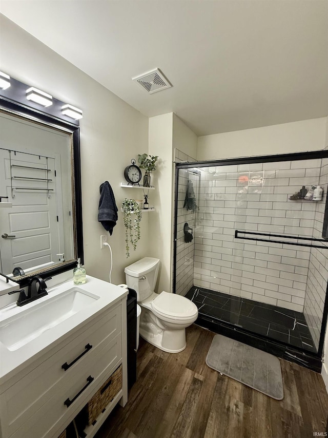 bathroom featuring a tile shower, vanity, wood-type flooring, and toilet