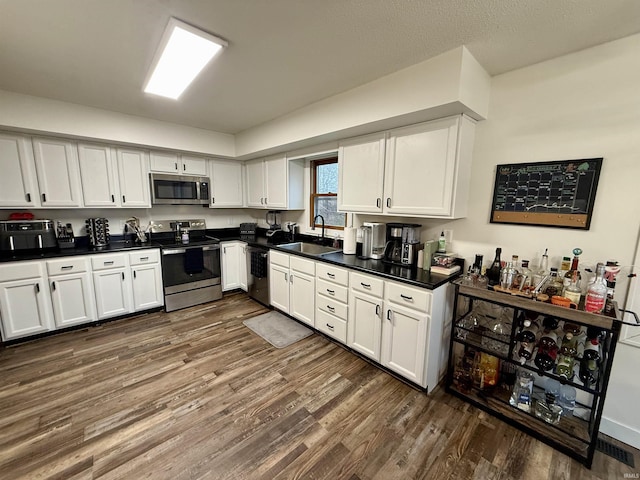 kitchen with white cabinets, appliances with stainless steel finishes, dark hardwood / wood-style floors, and sink